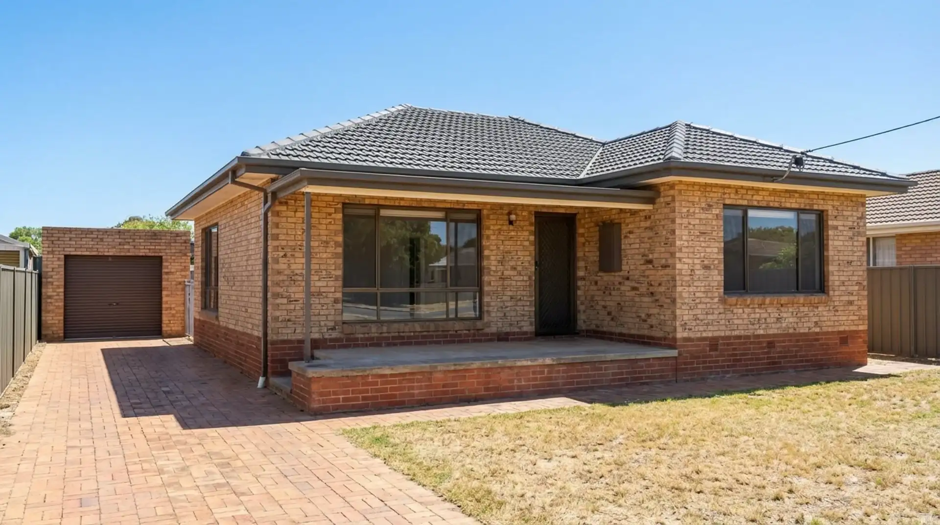 Brick house with tiled roof and paved driveway on a sunny day in suburban Australia